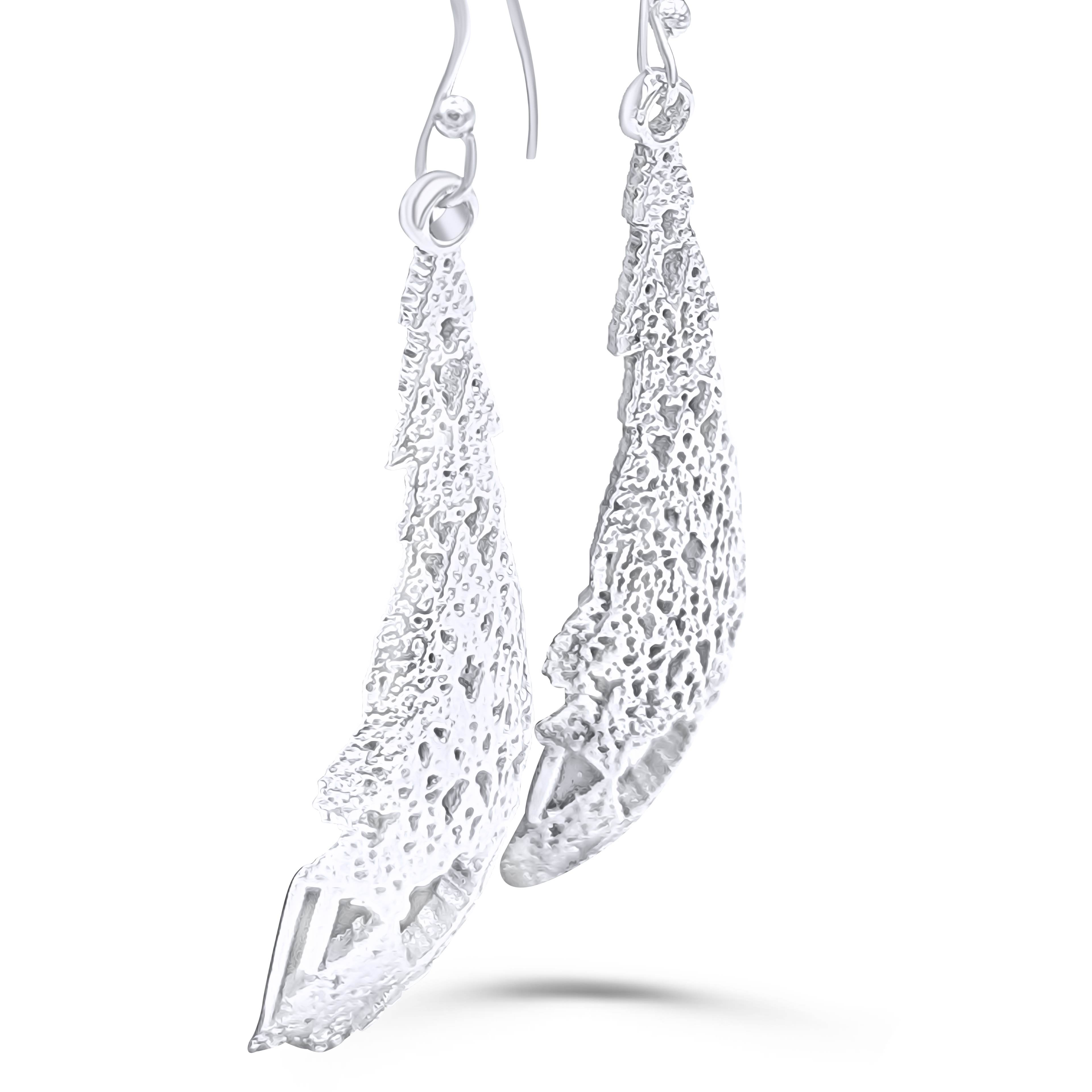 A pair of dangling silver earrings shown from the side
