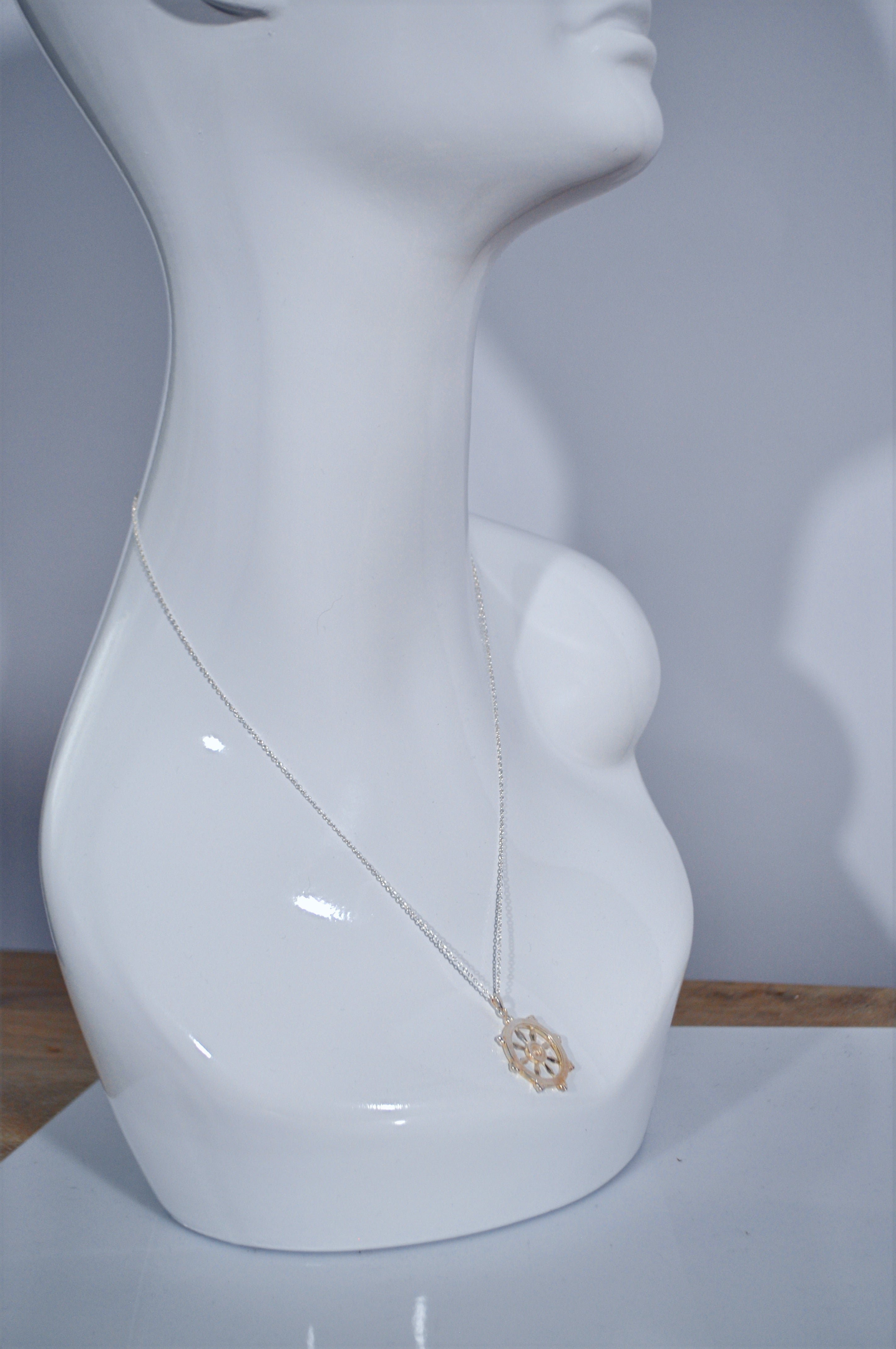 White mannequin head wearing a wheeled dharma wheel pendant on a plain background
