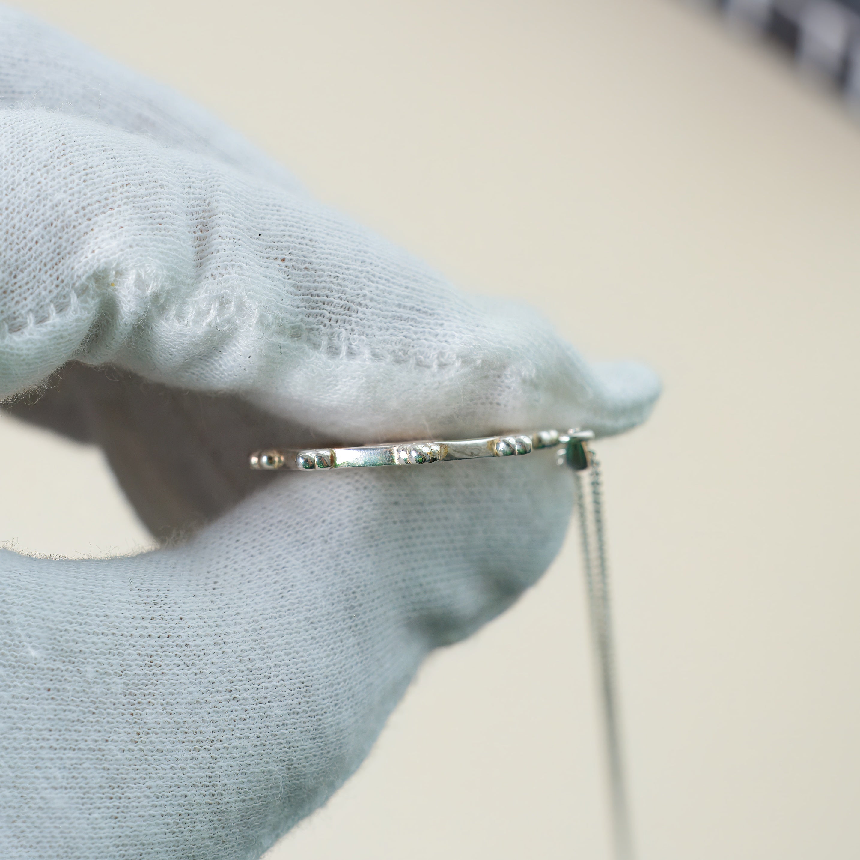 Silver bracelet held by a gloved hand on a neutral background