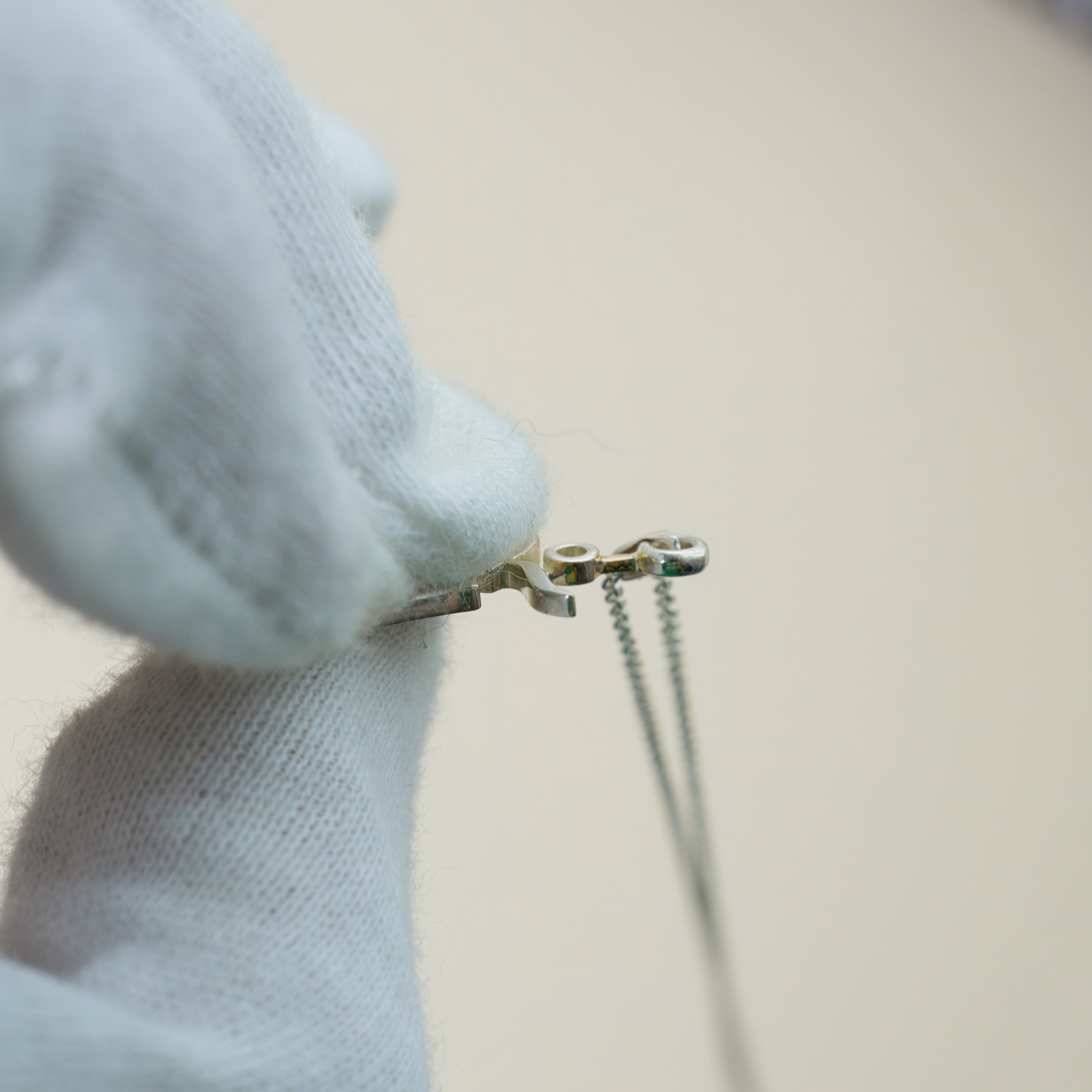 a silver tibetan om pendant helded by a white gloved hand, the pendant showing the side.