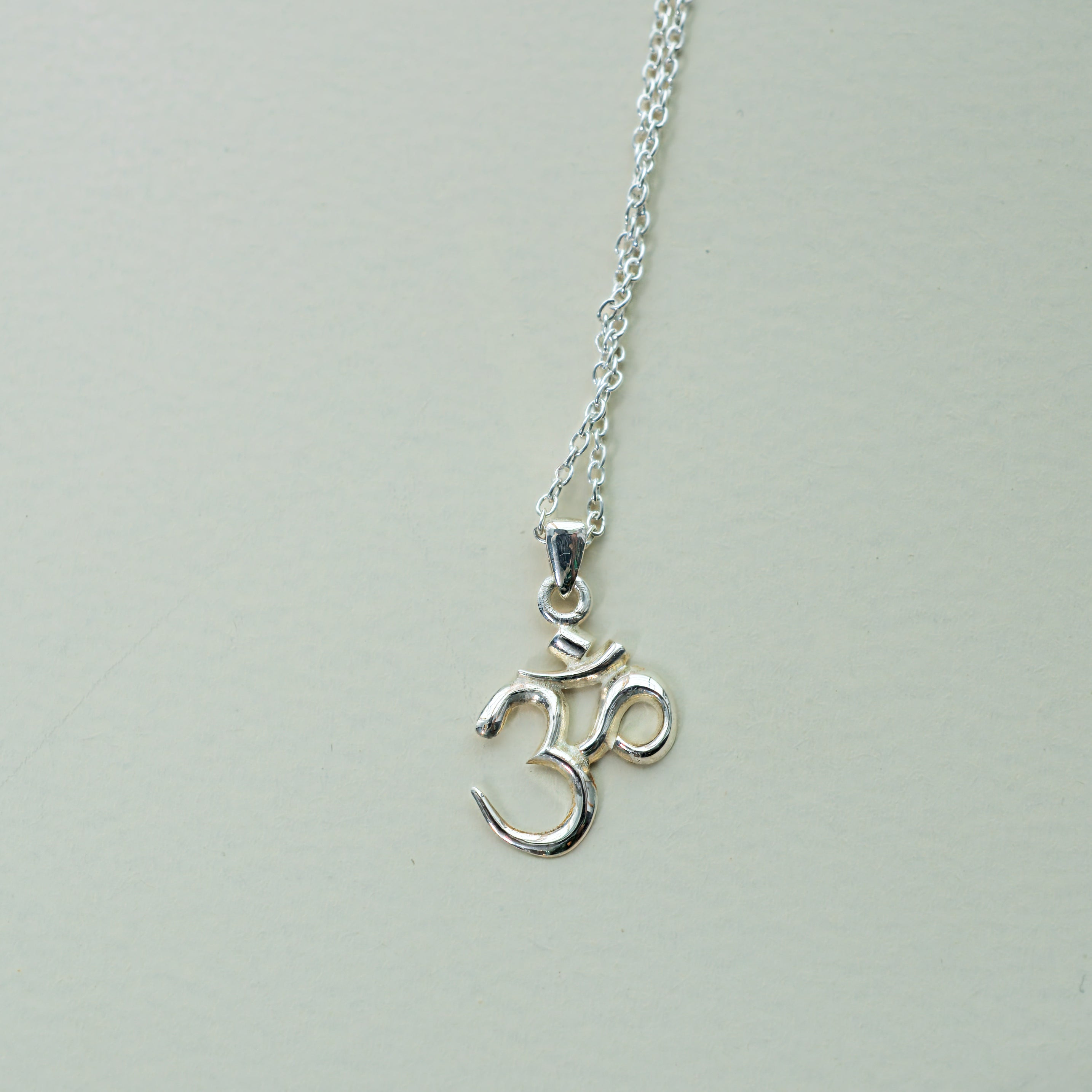 Silver necklace with an om symbol pendant on a light gray background