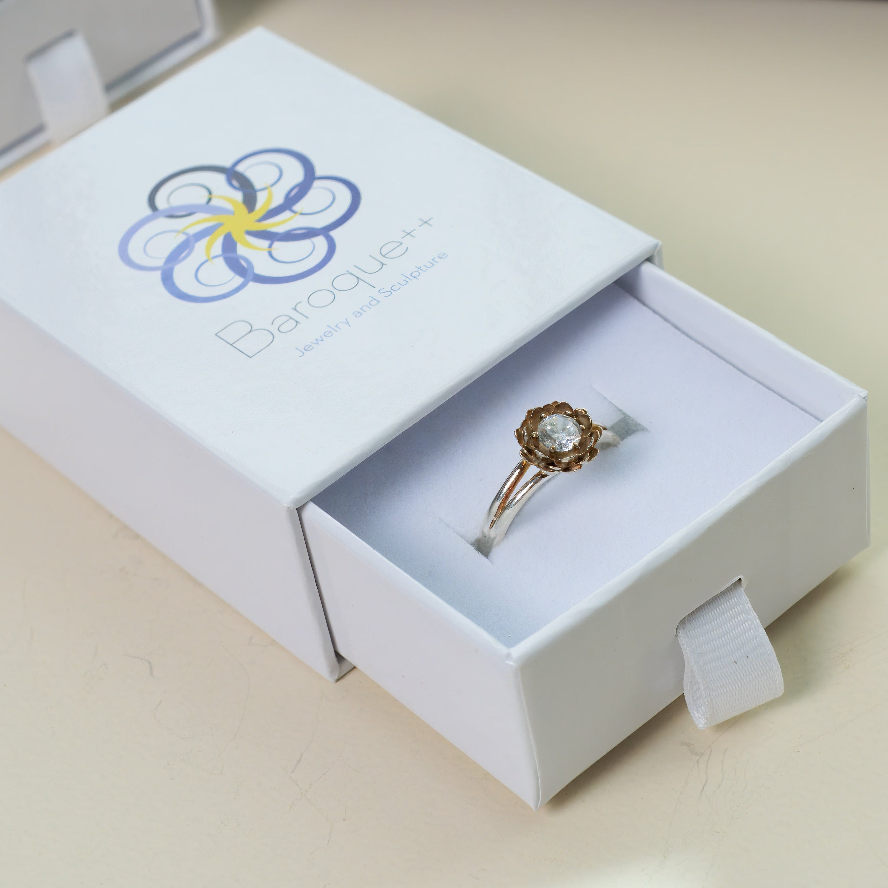 a silver ring in a jewelry box with logo on cream-colored background