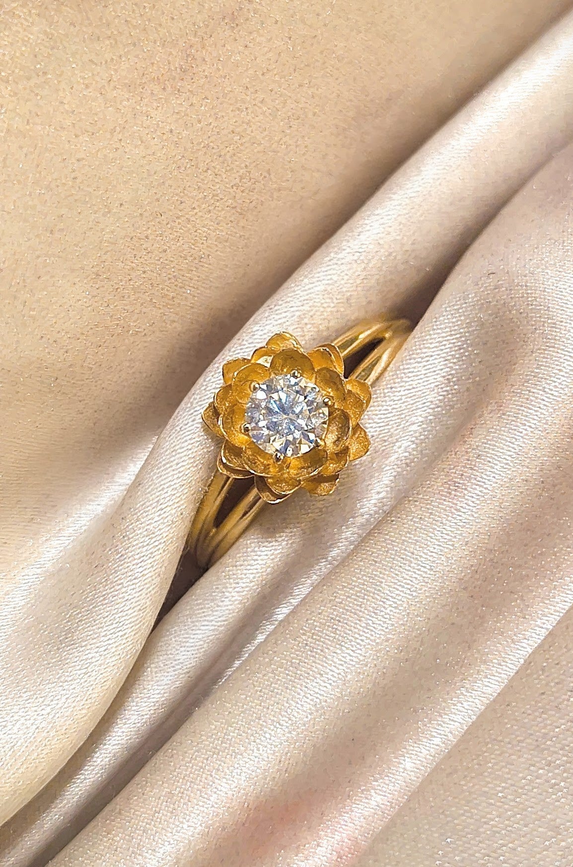 a gold ring with solitaire diamond on gold cloth