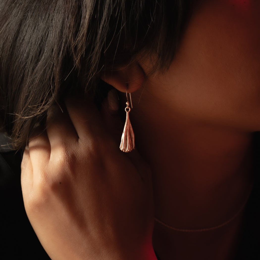 Close-up of a person wearing a silver tassel earring against a dark background