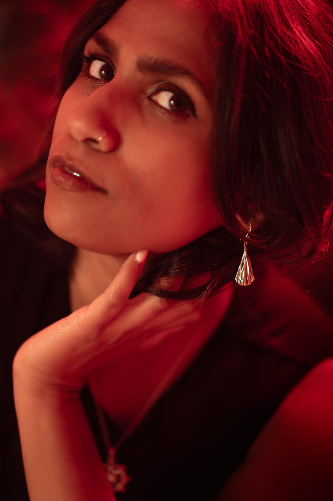 a woman wearing earrings with black hair and a red light and red background