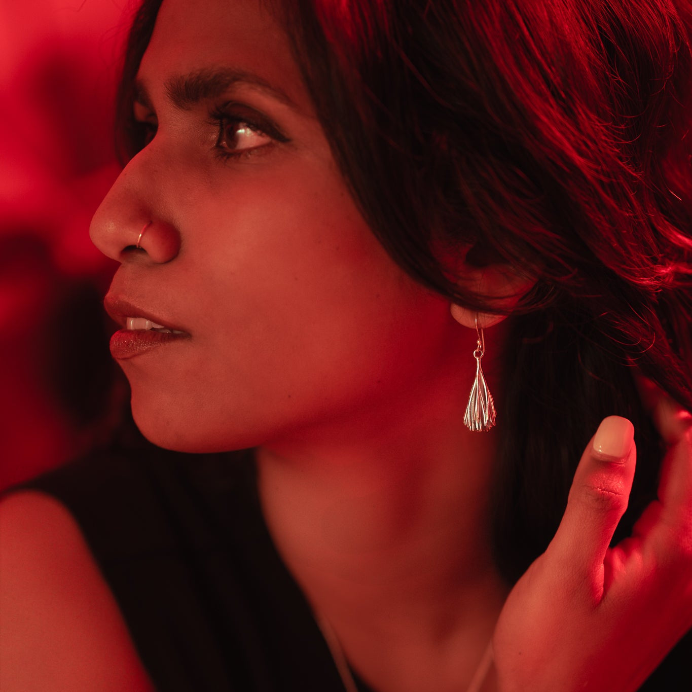 Woman with a red background wearing a black top and silver earring.