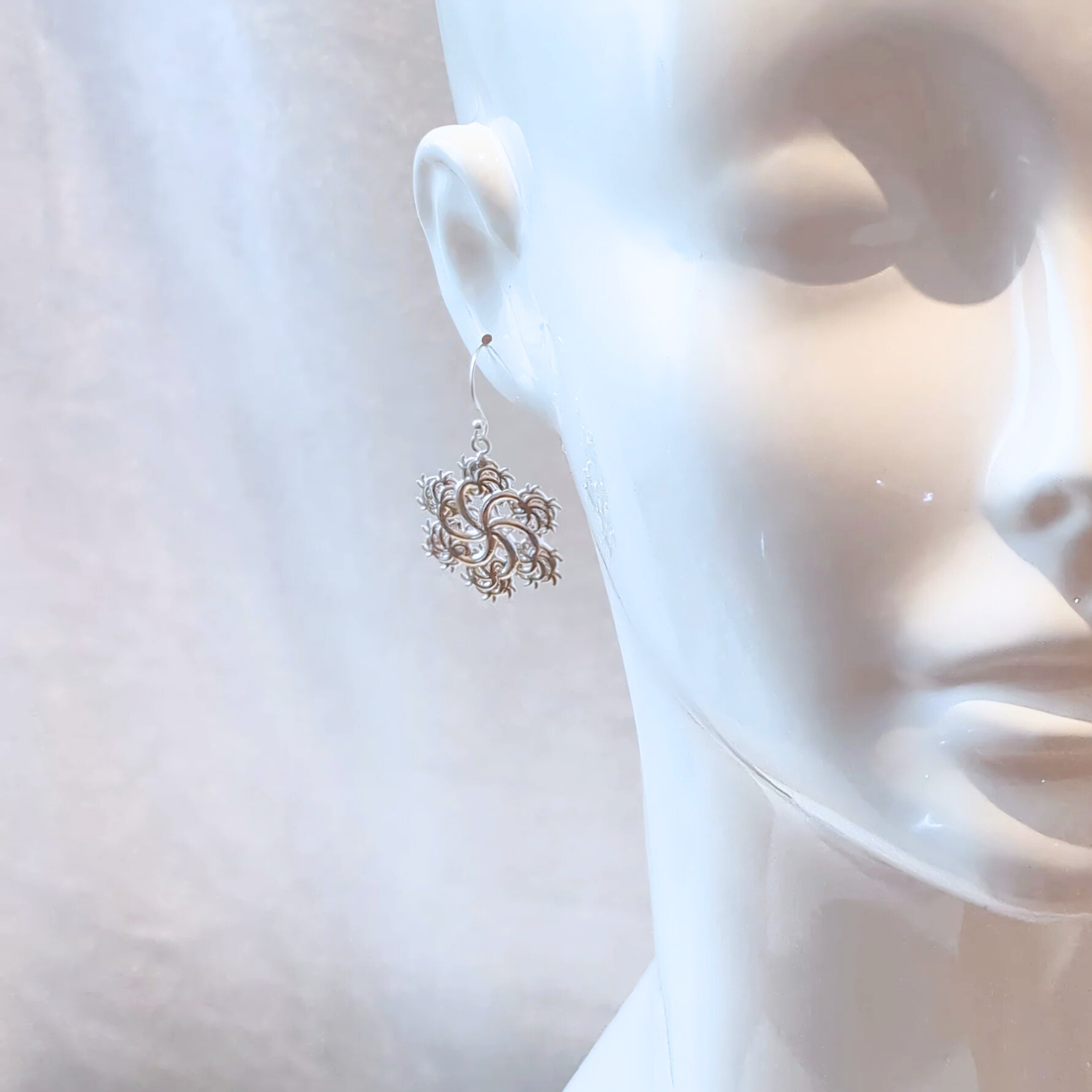 Half a mannequin's face wearing a six-pointed earring on the right ear in front of a white background