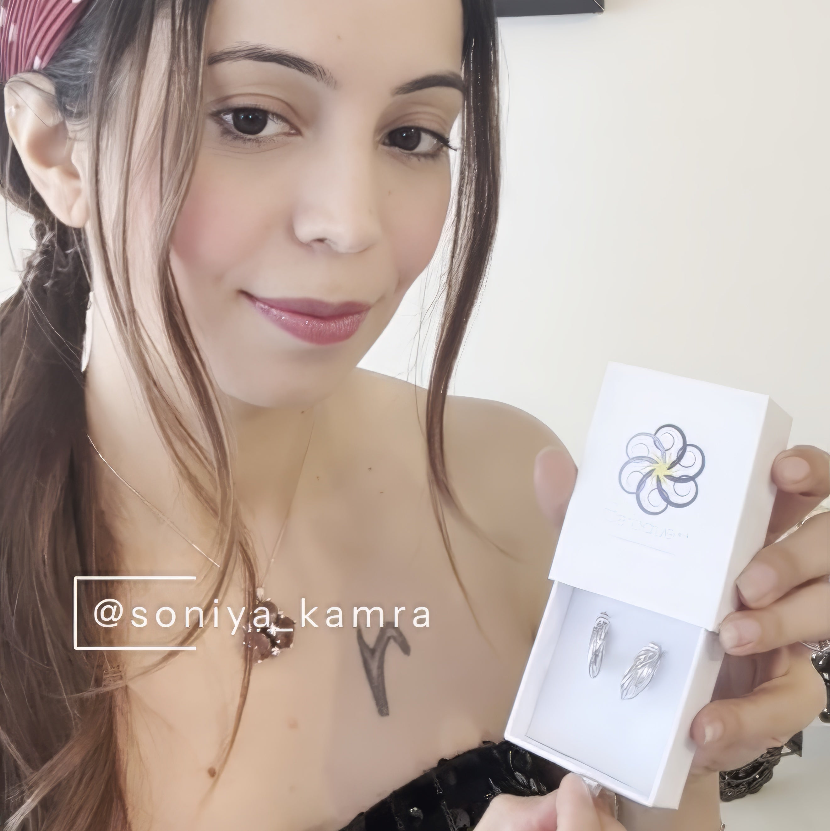 woman holding box of hoop earrings with logo on the box and white wall behind.