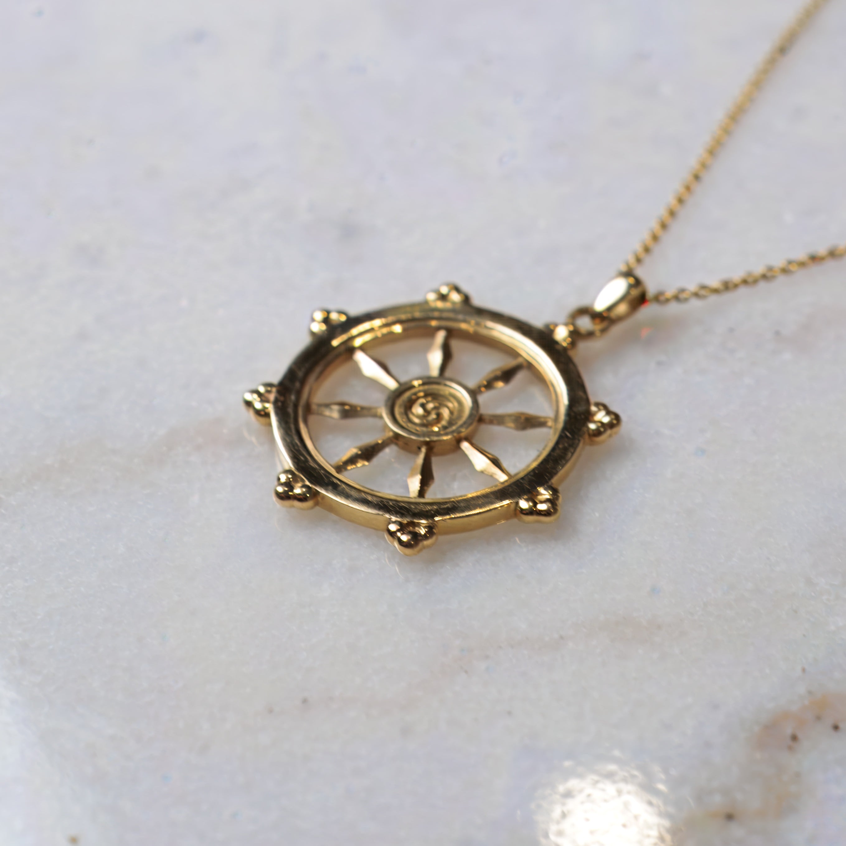 Gold necklace with a round dharma wheel pendant on a marble surface