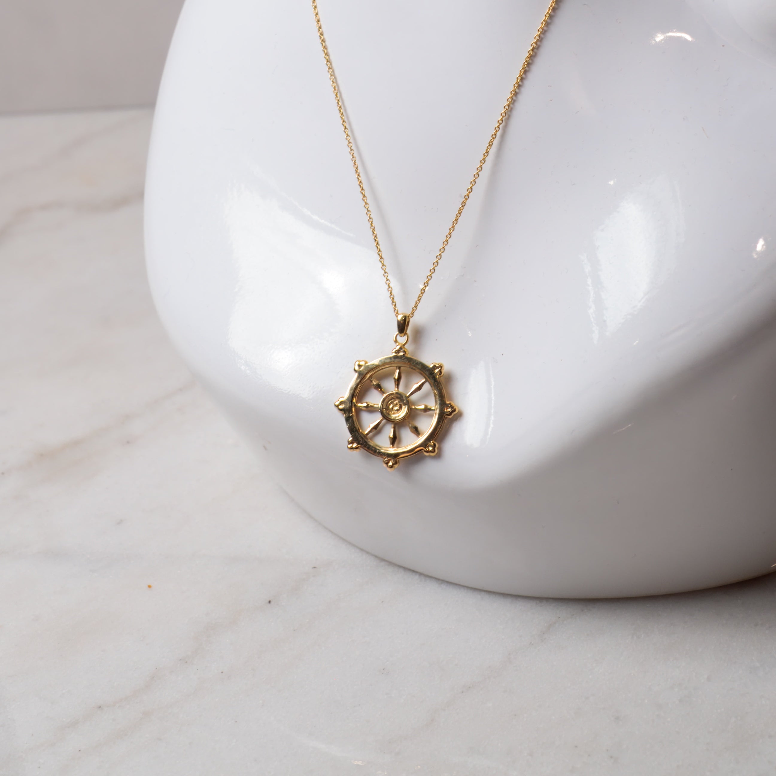 Gold necklace with a decorative dharma wheel pendant on a white mannequin bust.