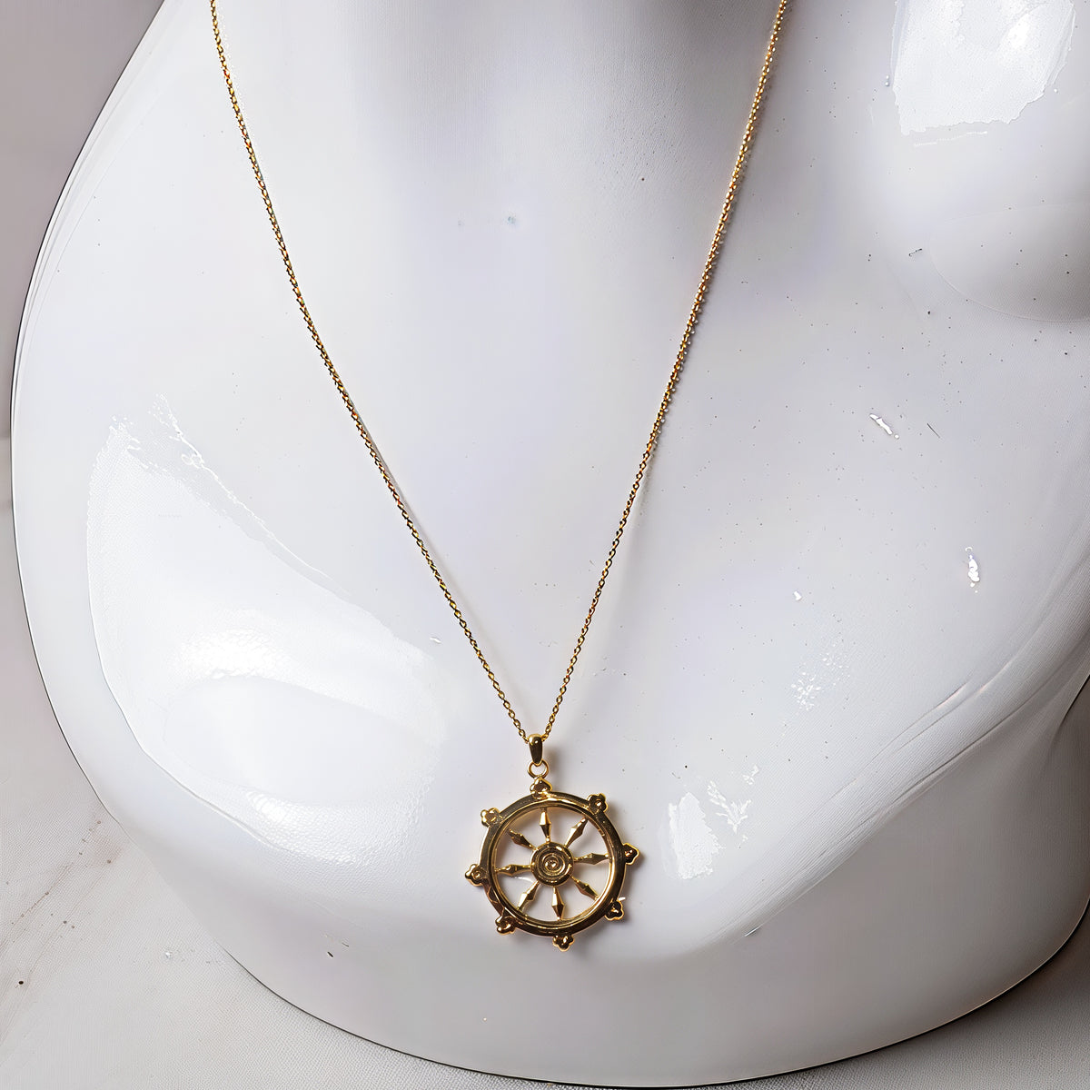 Gold dharma wheel pendant on a mannequin, alternate view