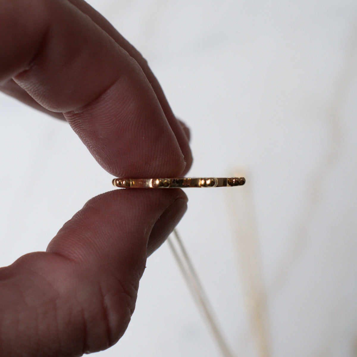 Gold dharma wheel pendant held between fingers, showing its thickness
