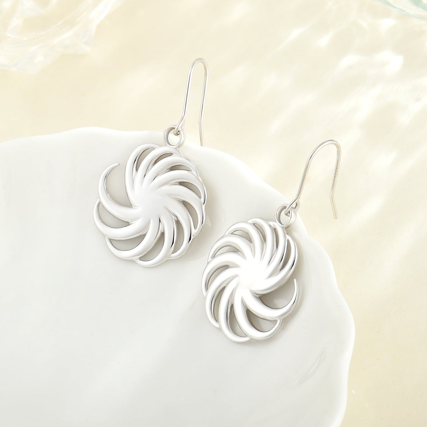 Silver earrings with a swirling design on a white surface
