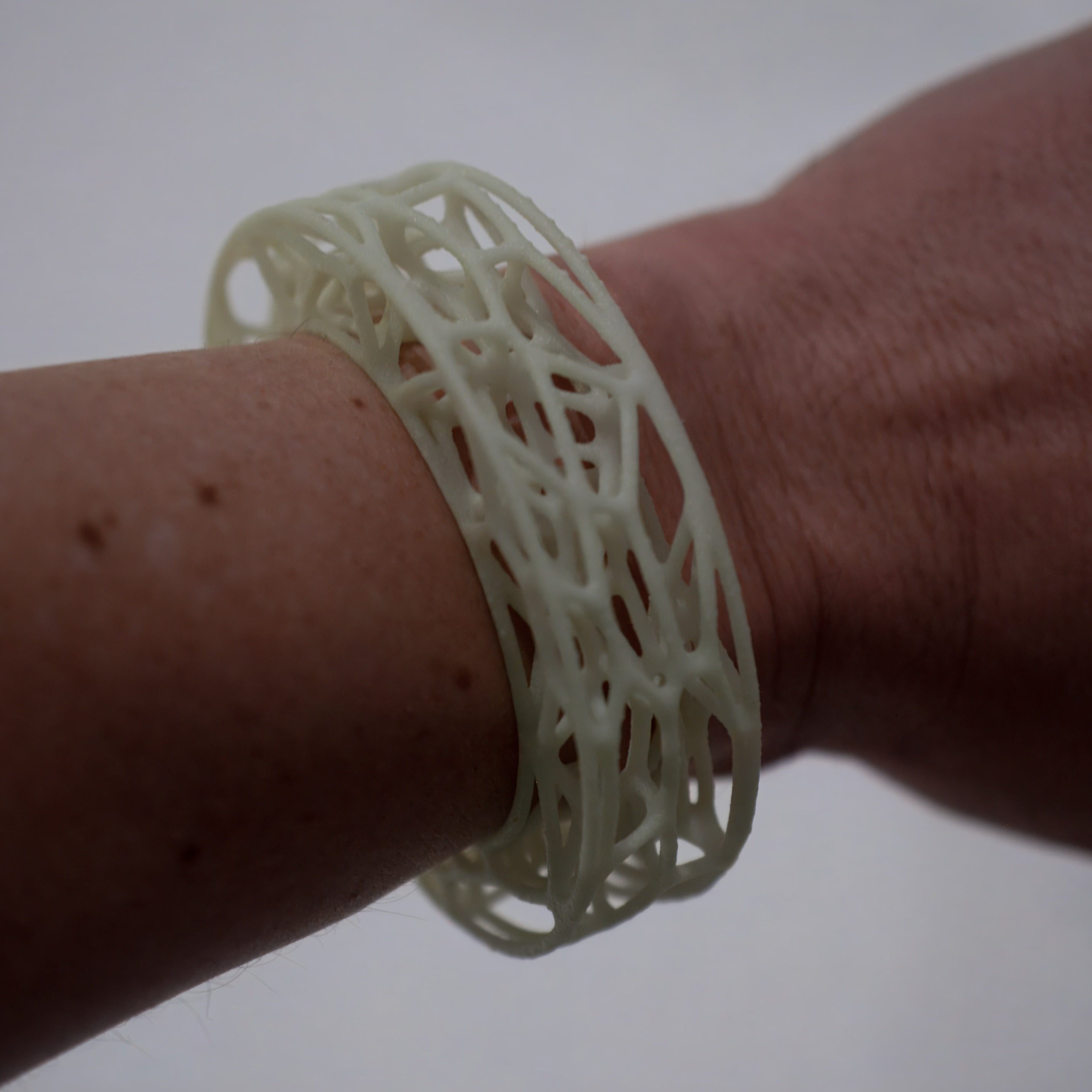 Close-up of a wrist wearing a white, intricately designed bracelet against a plain background