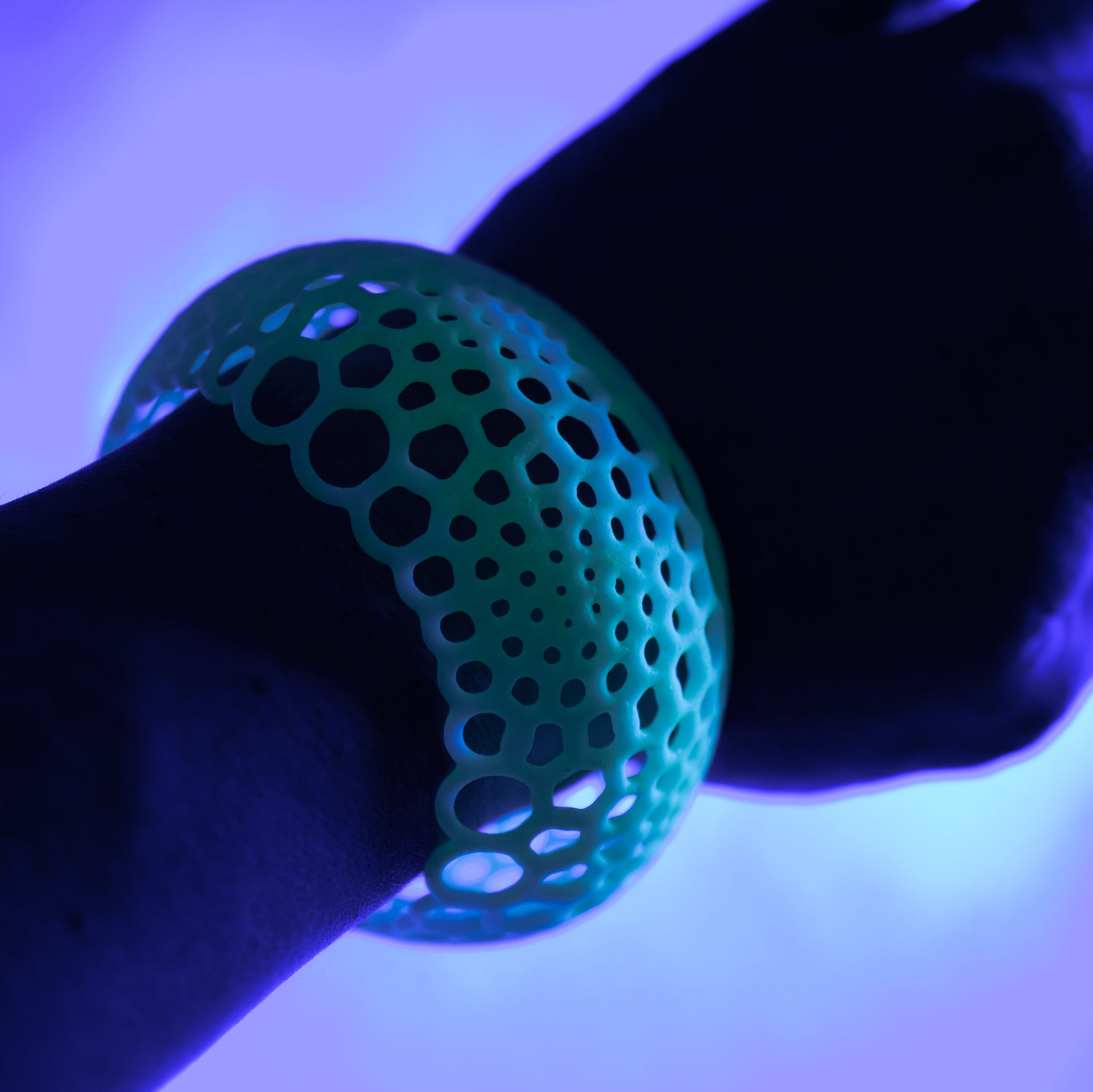 a glowing green bracelet on a wrist under a purple blacklight