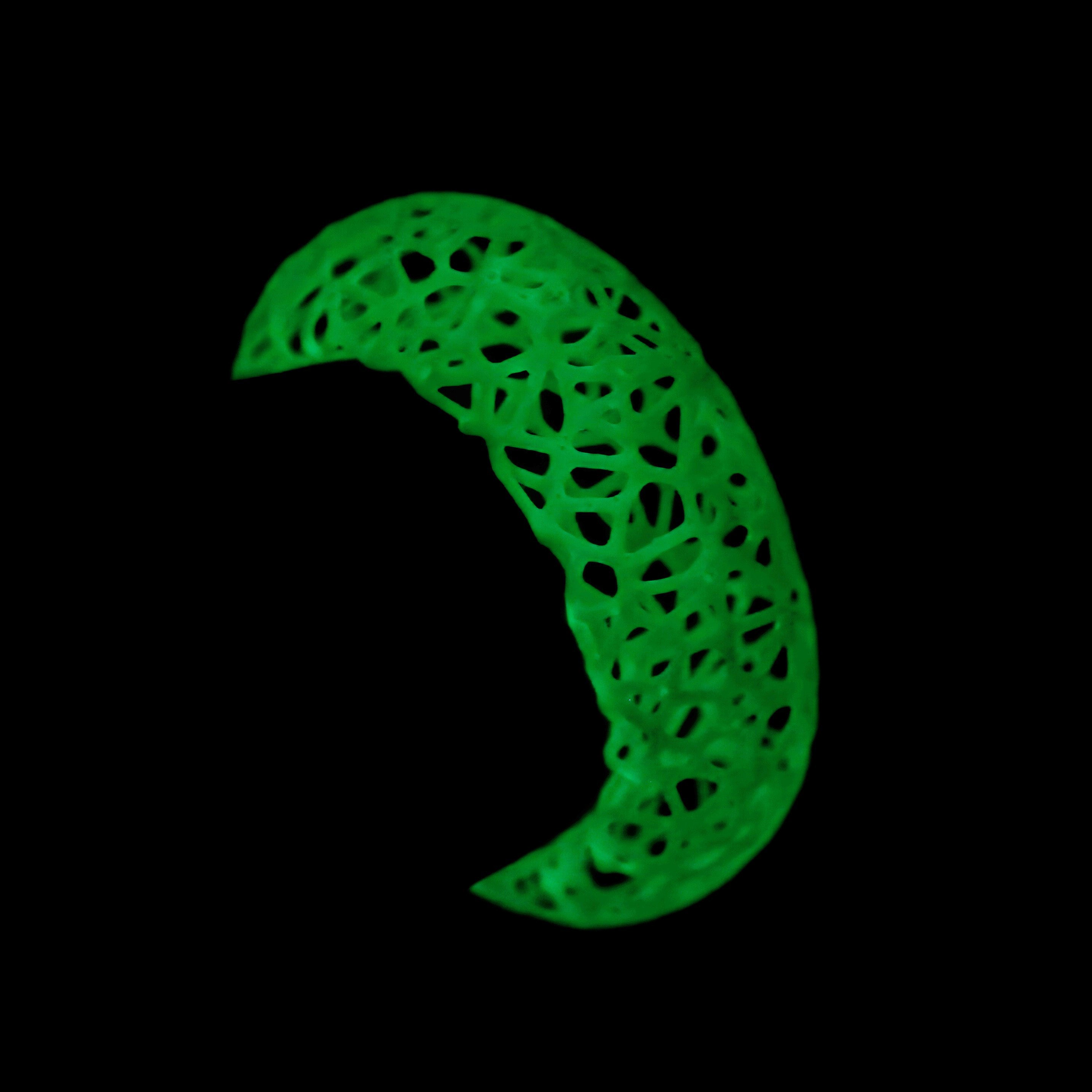 a glowing green cuff bracelet with intricate design on a wrist in the dark.