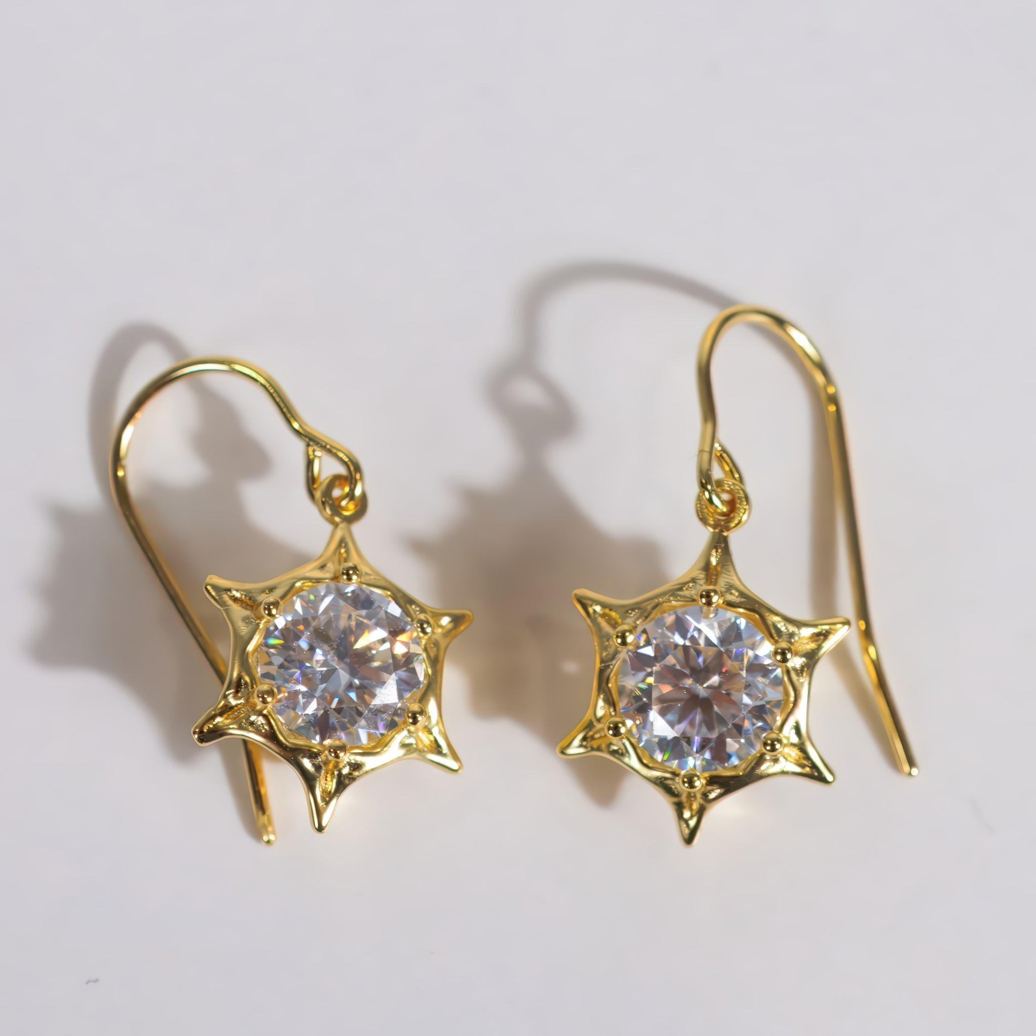 A pair of gold star-shaped dangle earrings with clear round-cut gemstones, displayed on a plain white background with soft shadows.