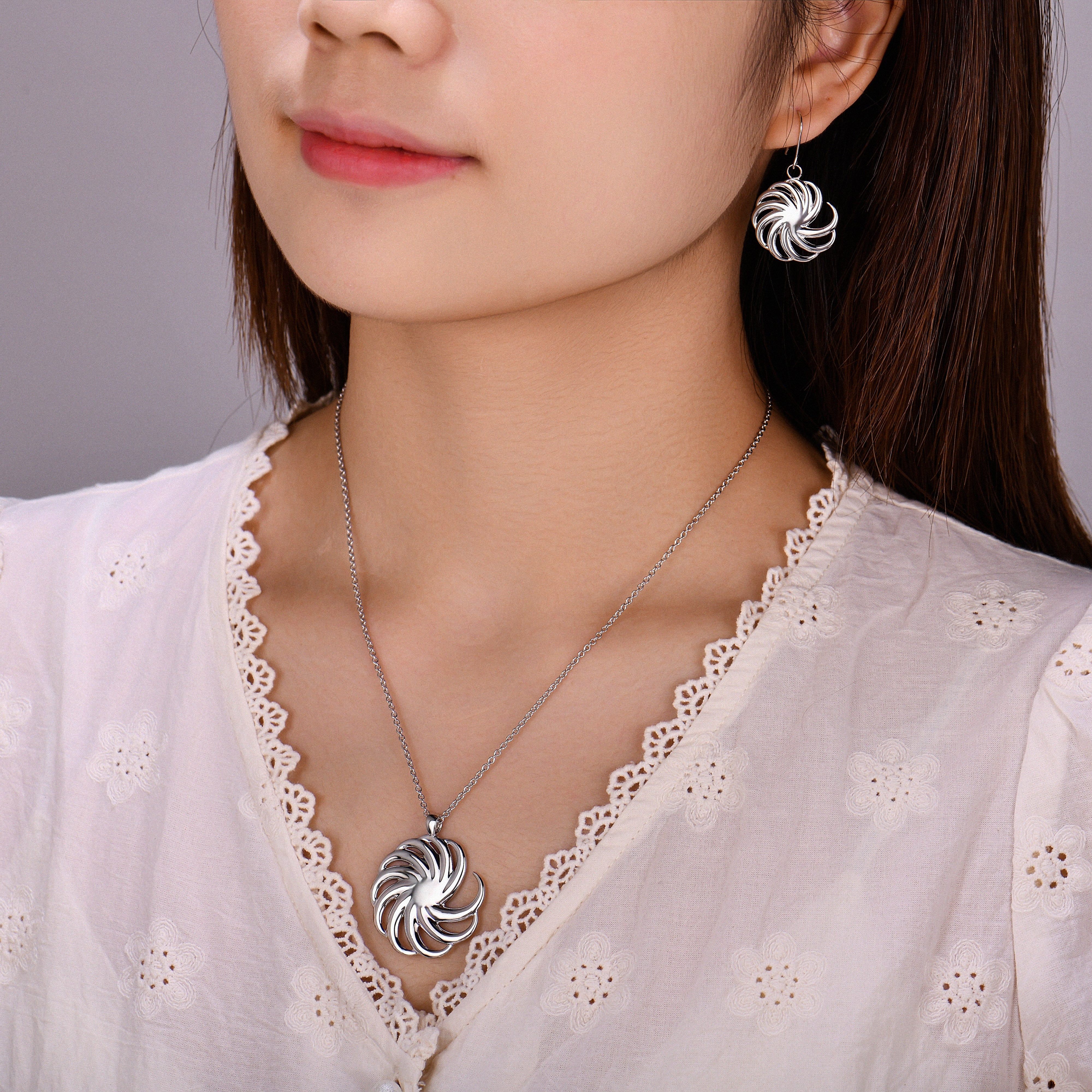 Woman wearing silver spiral earrings and matching necklace with a plain background