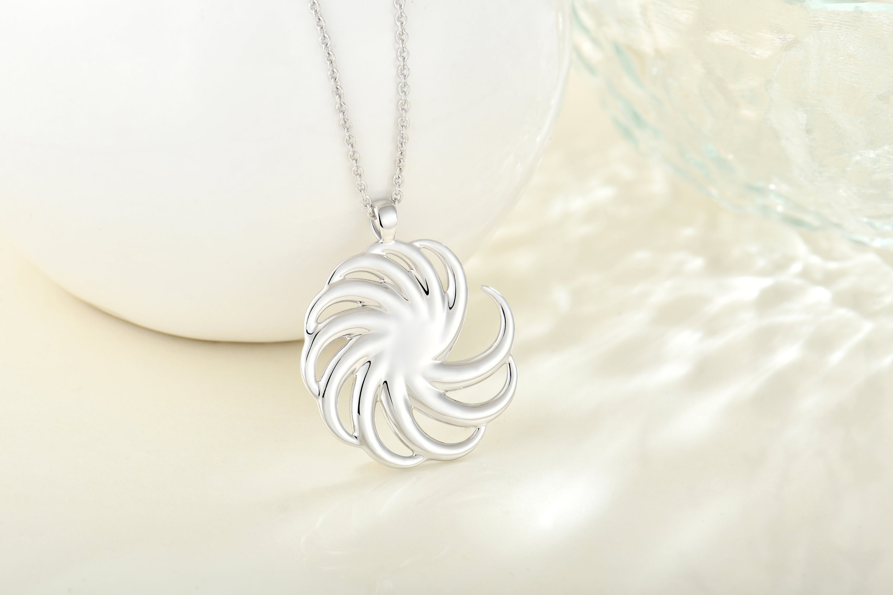 a sterling silver round spiral pendant with silver chain on a pearl white background