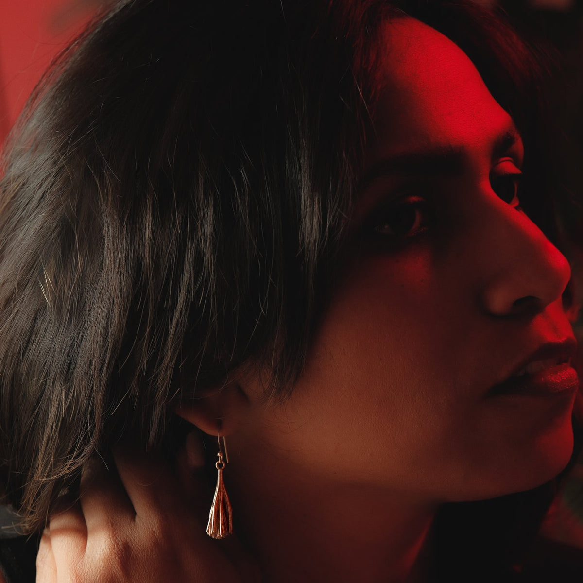 Close-up of a Palpae tassel earring worn against a dark red background