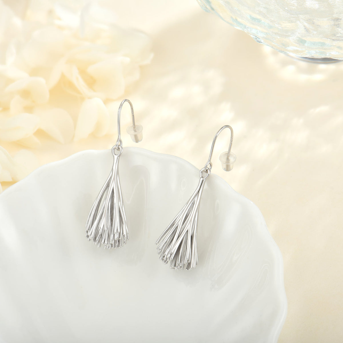 Silver Palpae tassel earrings on a white scalloped dish with flowers