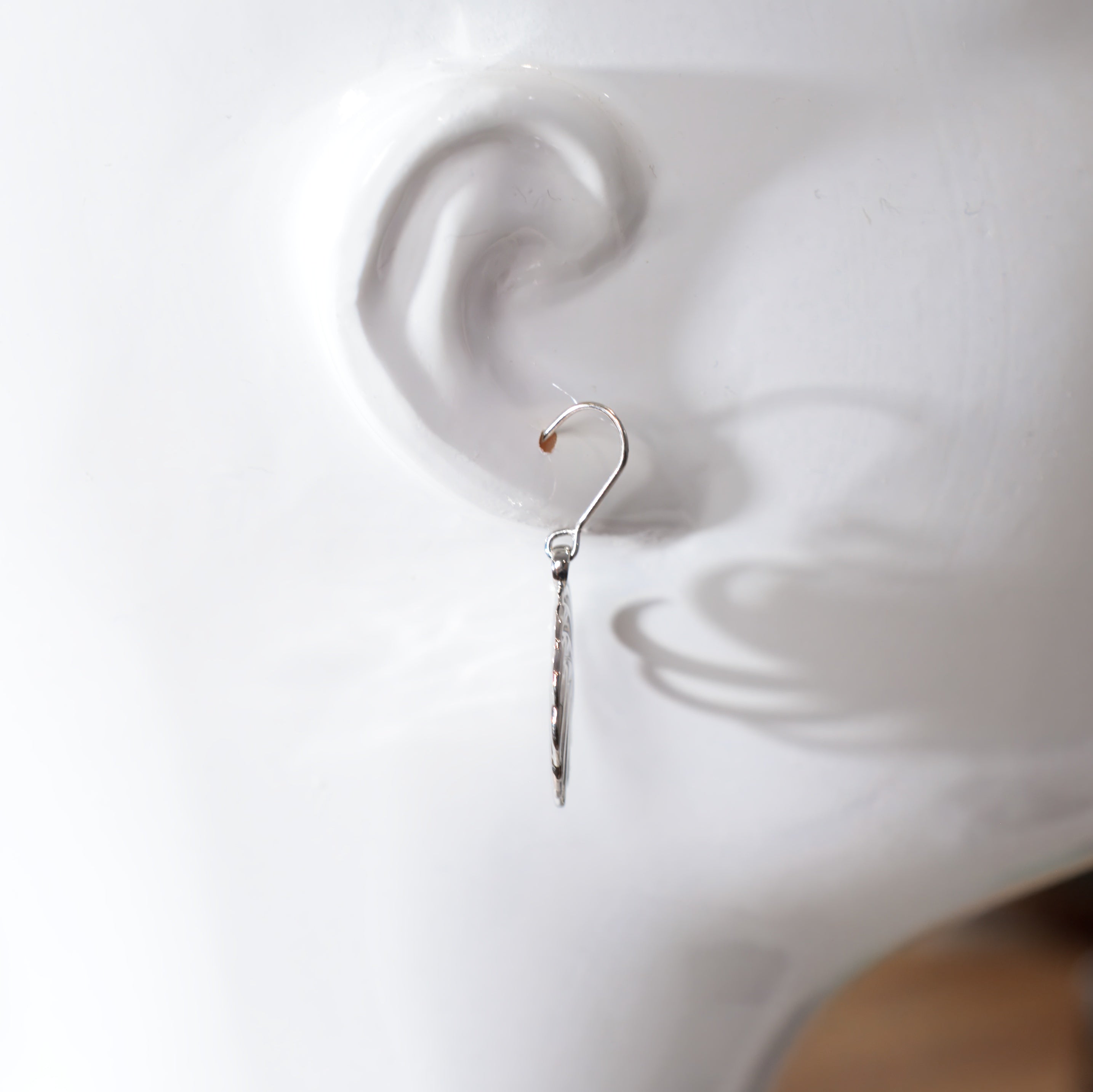 side view of silver earrings being worn on a white mannequin ear with a plain background