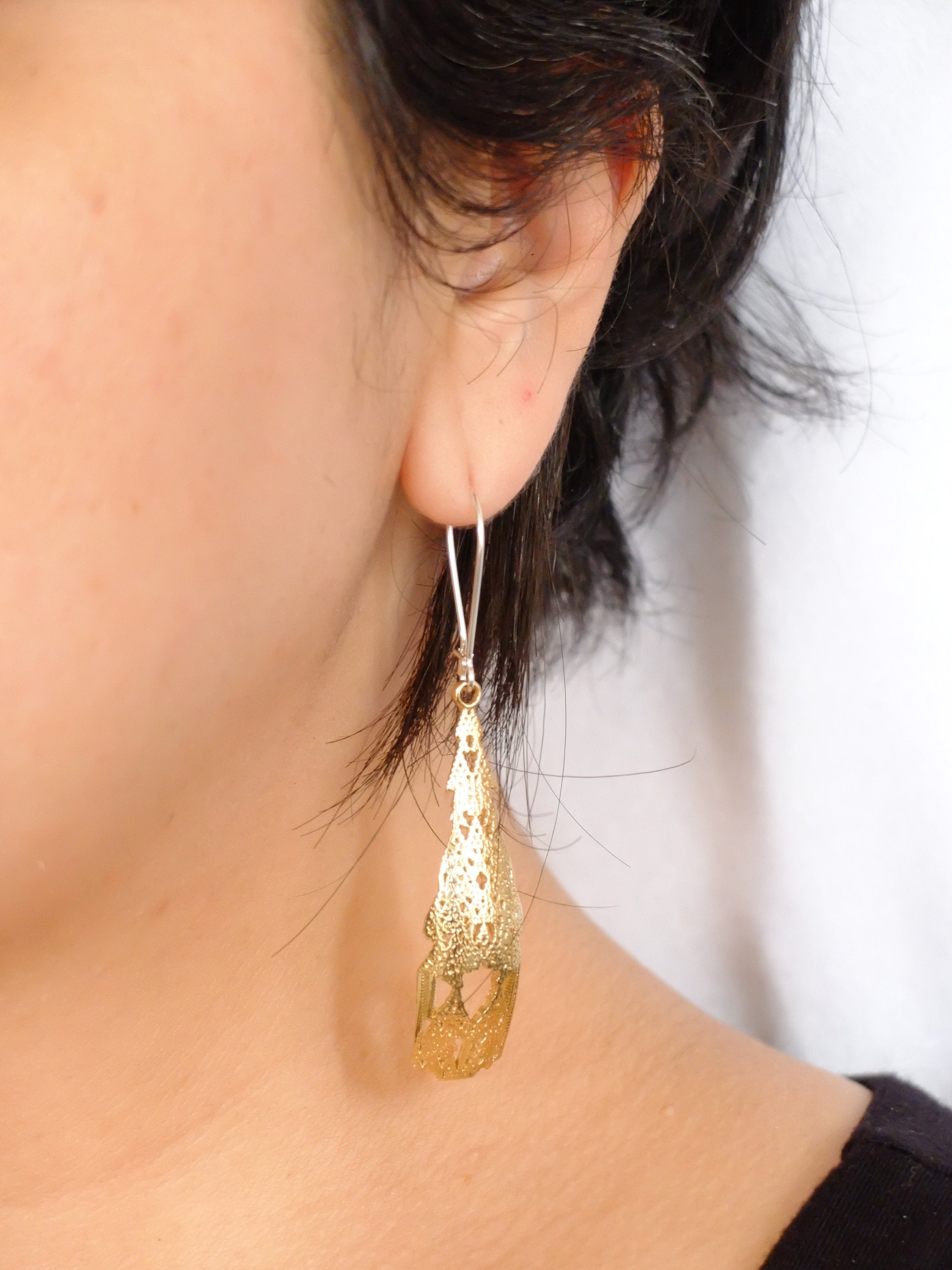 A single dangling earring with an intricate organic design, appears gold-colored, displayed against a light background.