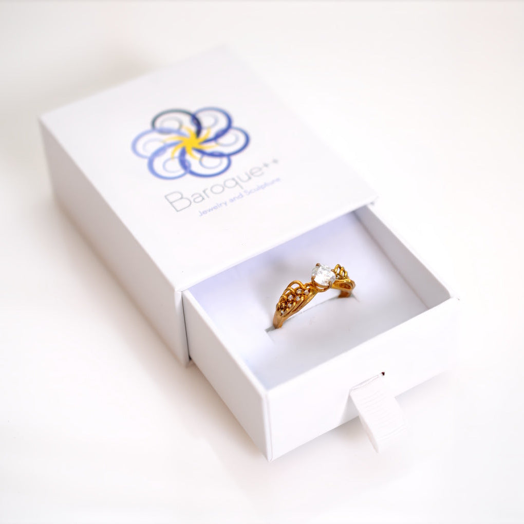 Gold ring in a white box with a brand logo on a white background