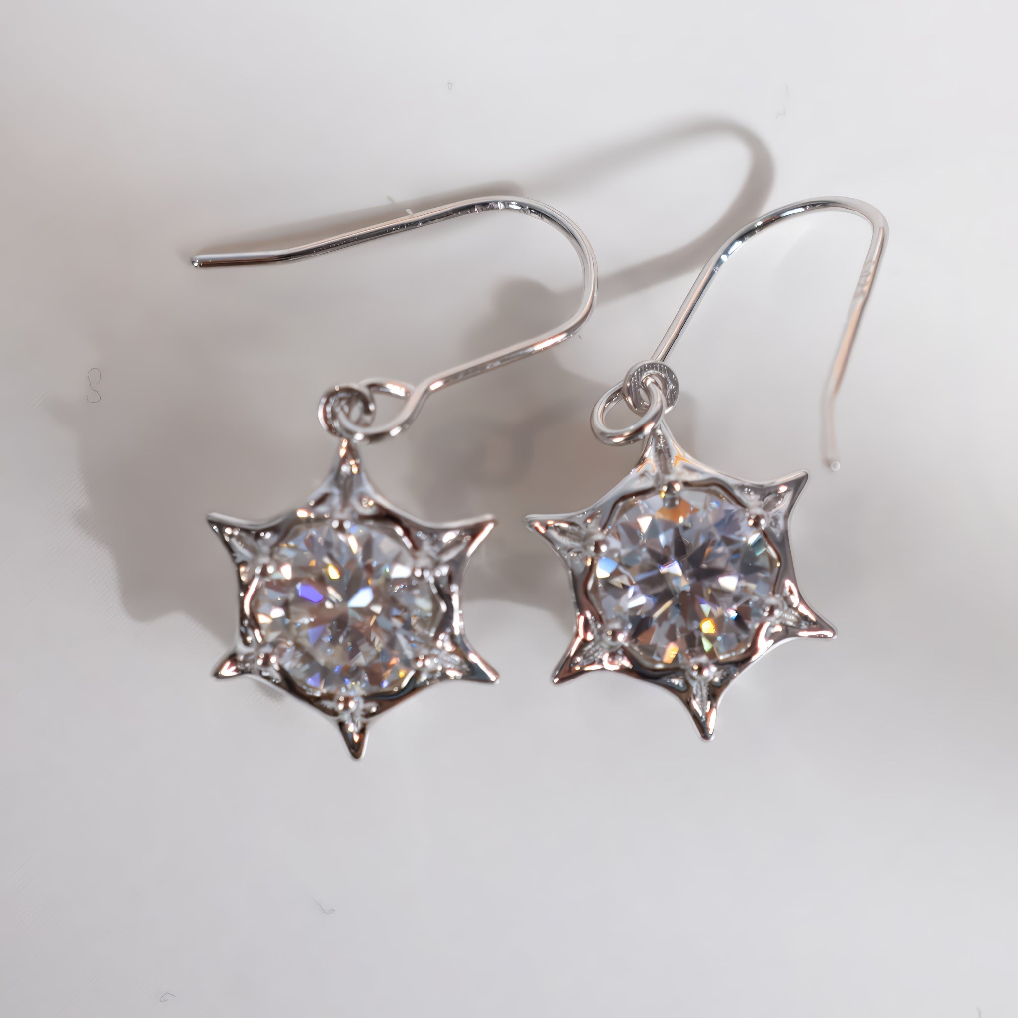 A pair of silver-tone dangle earrings with six-pointed starburst settings holding round clear faceted gemstones, photographed on a plain light background.