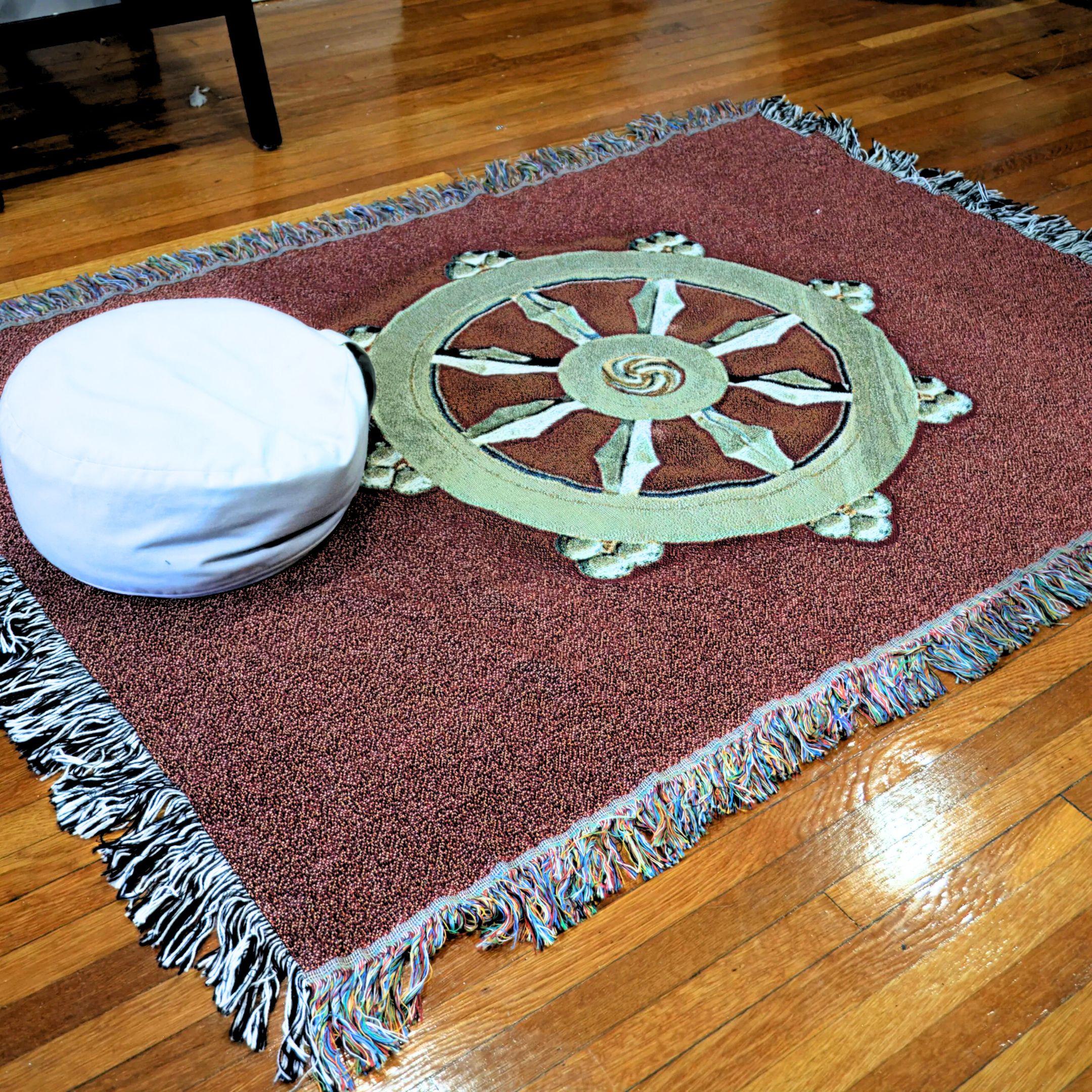 meditation pillow sitting on red blanket with gold dharma wheel on wood floor