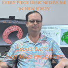 A picture of a man with glasses at a desk. Behind him on the left monitor is an image of a web-like bracelet. On the right monitor is a visual programming interface and a green twisting geometry. The text says "Every Piece Designed by Me in New Jersey. Small Batch Not Mass Produced."