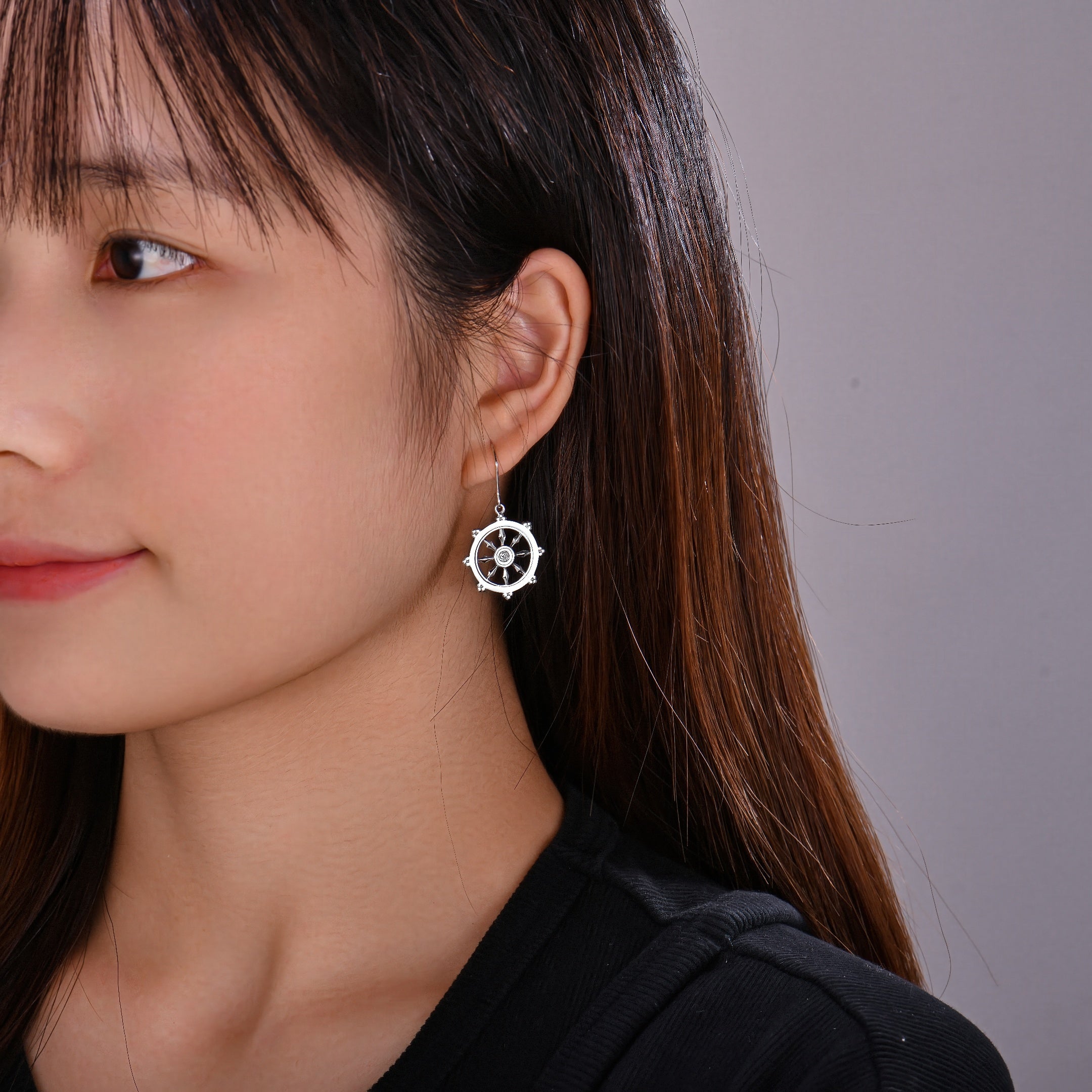 Close-up of a woman wearing a sterling silver dharma wheel earring against a neutral background