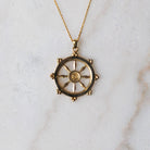 Gold dharma wheel necklace with a decorative pendant on a marble surface