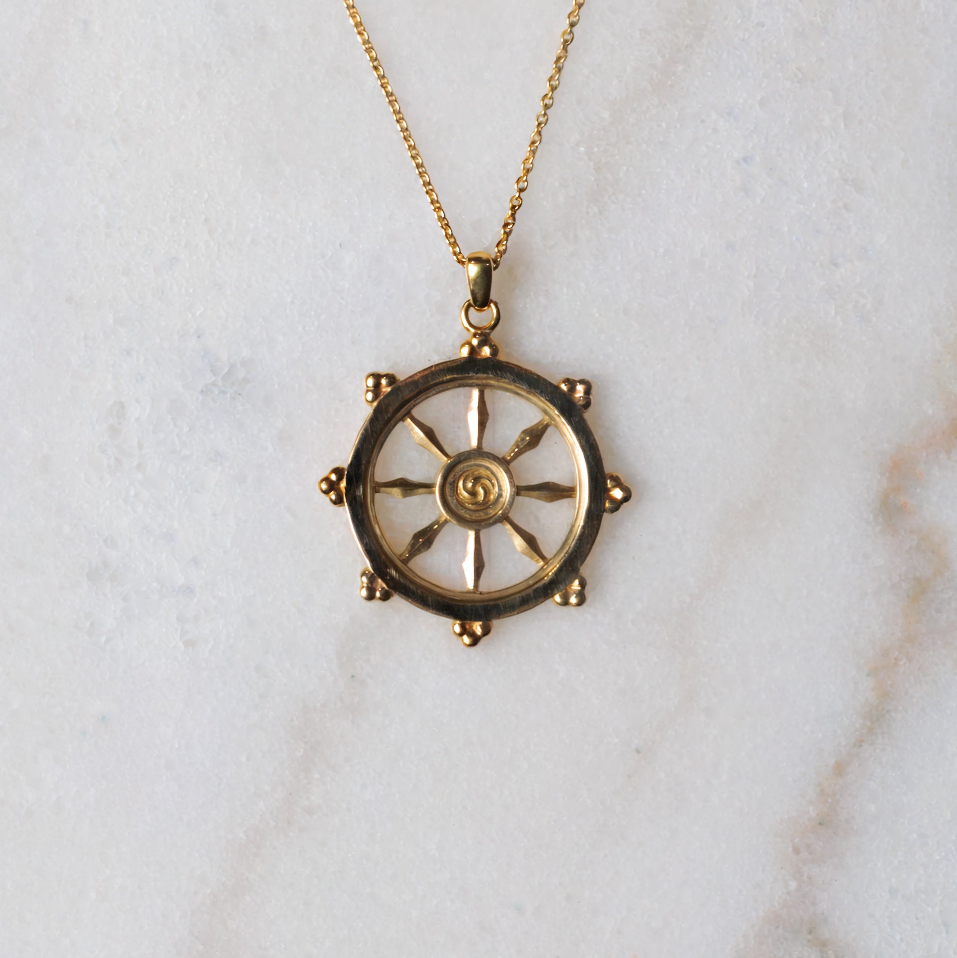 Gold dharma wheel necklace with a decorative pendant on a marble surface