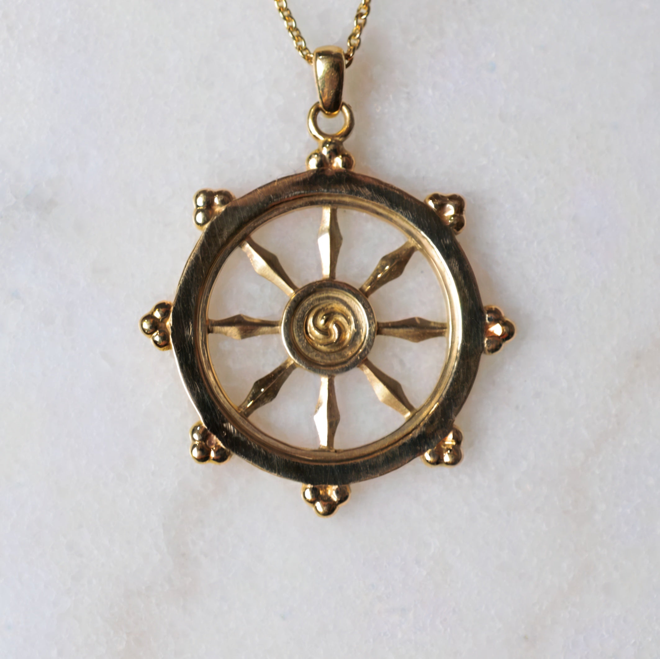 Gold necklace with a decorative wheel pendant on a white background