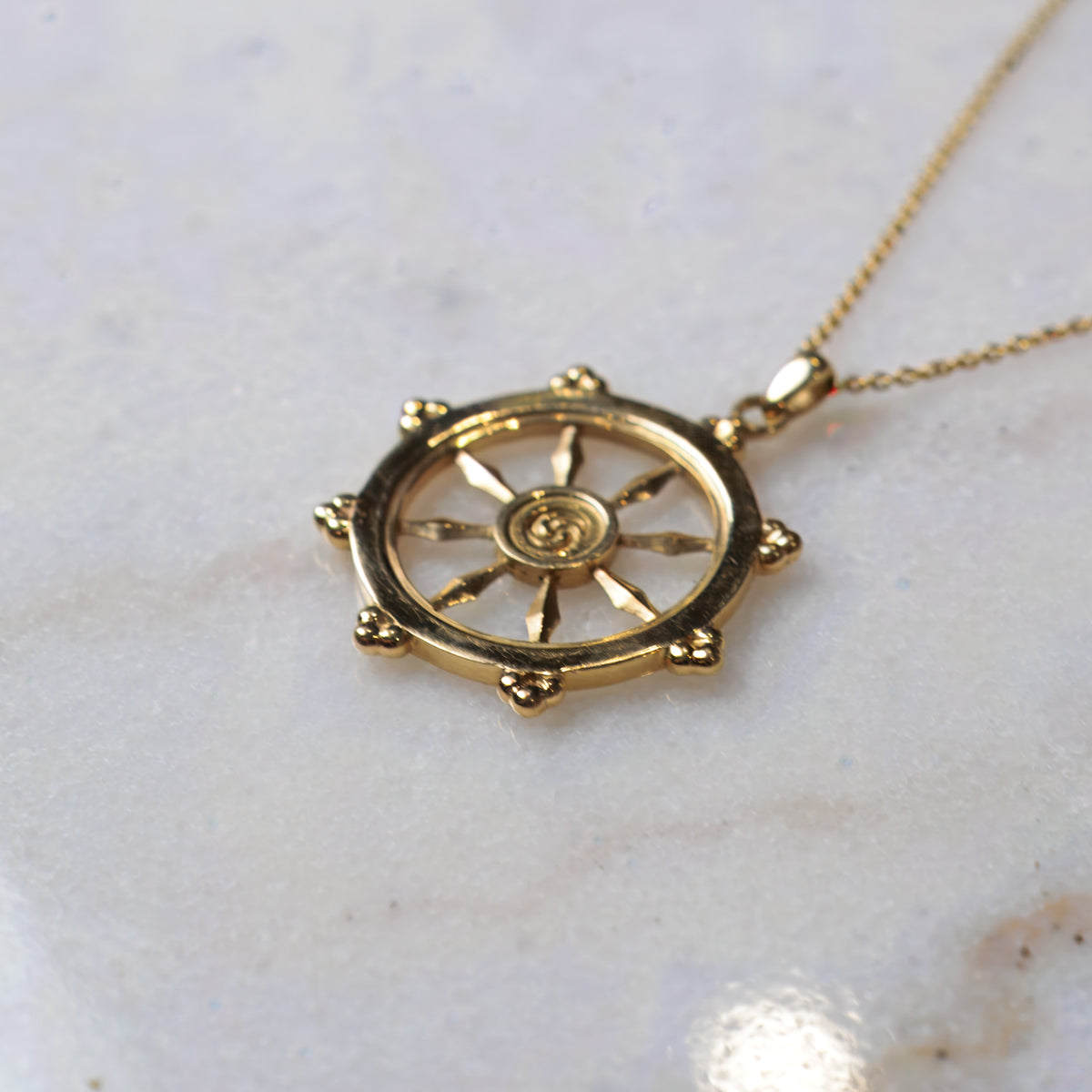 Solid gold dharma wheel pendant on marble