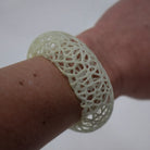 Close-up of a hand wearing a white, intricately designed bracelet on a light background