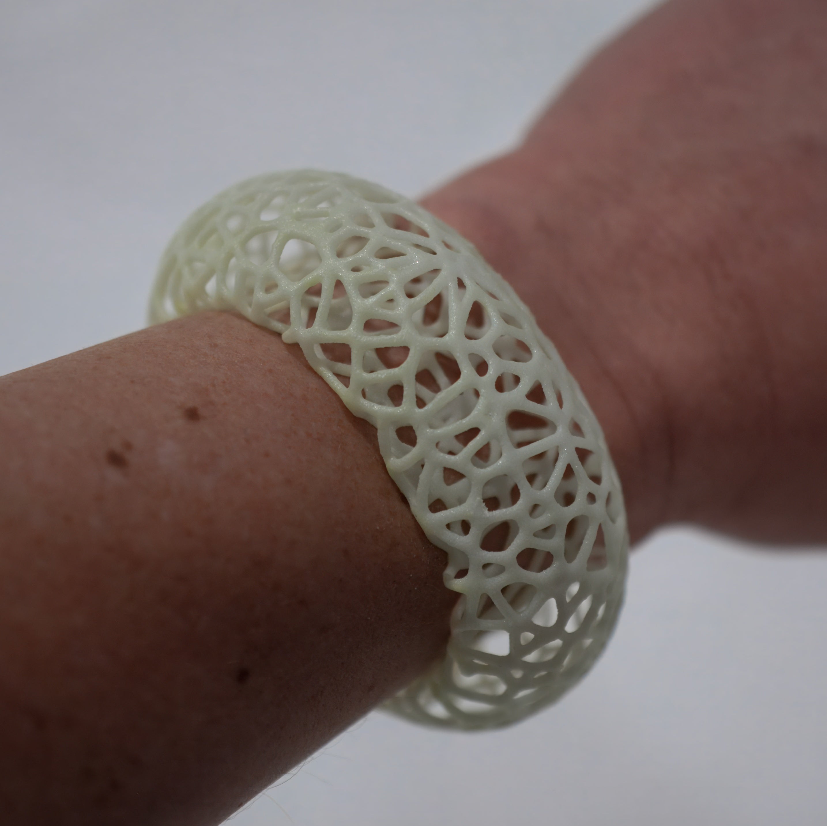 Close-up of a hand wearing a white, intricately designed bracelet on a light background