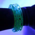 Green bracelet with a unique pattern on a wrist under a blue light