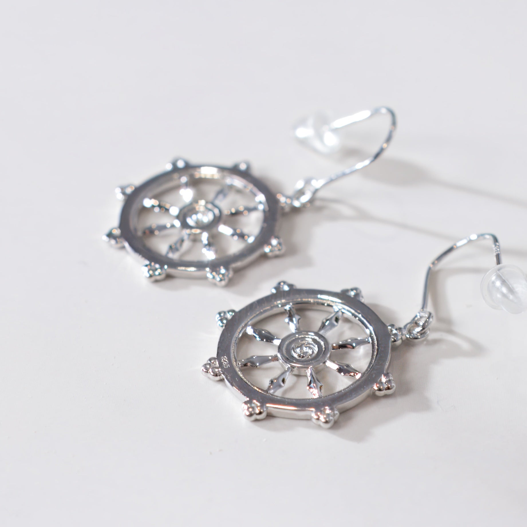 Silver steering wheel-shaped earrings on a light gray background
