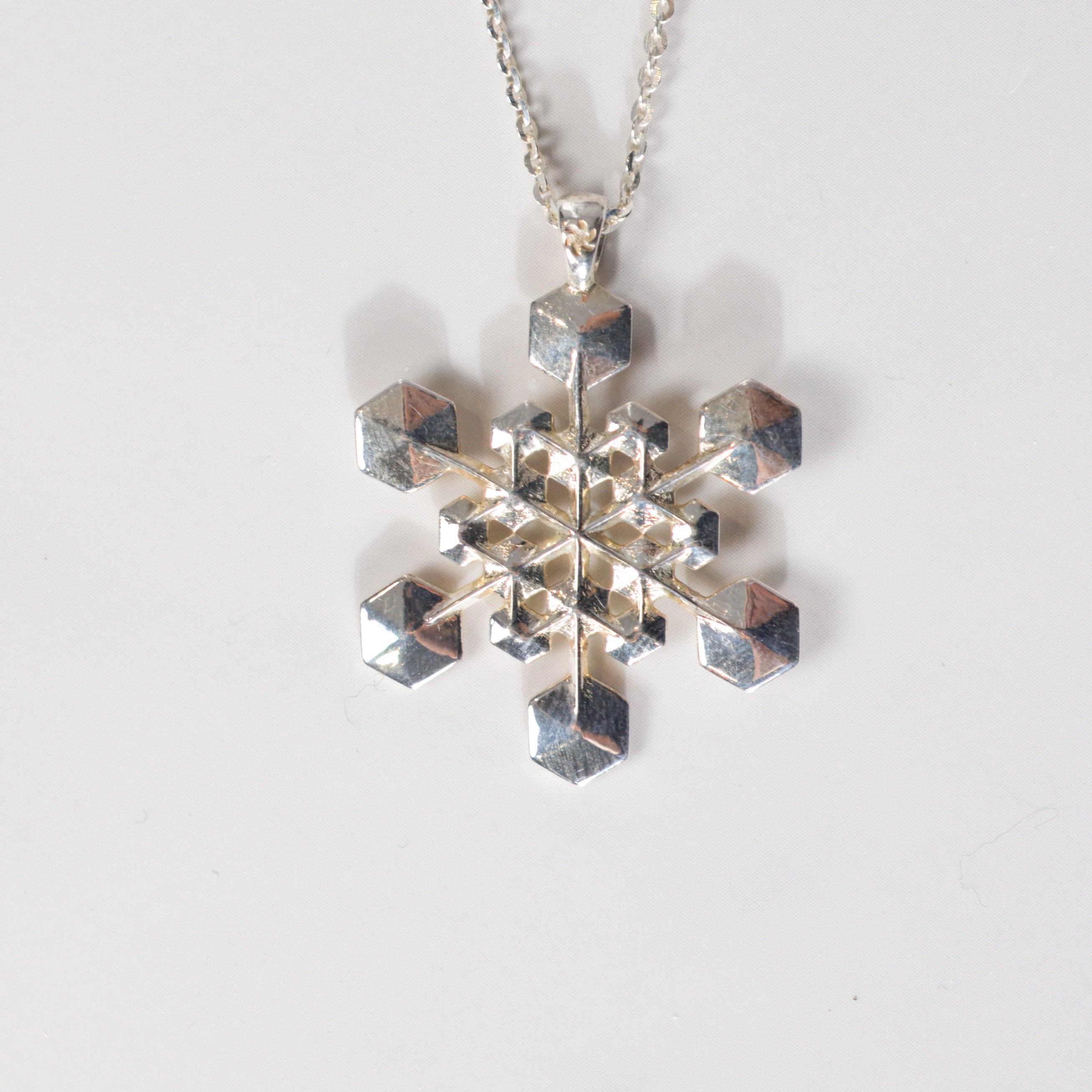 Silver snowflake pendant on a chain against a white background