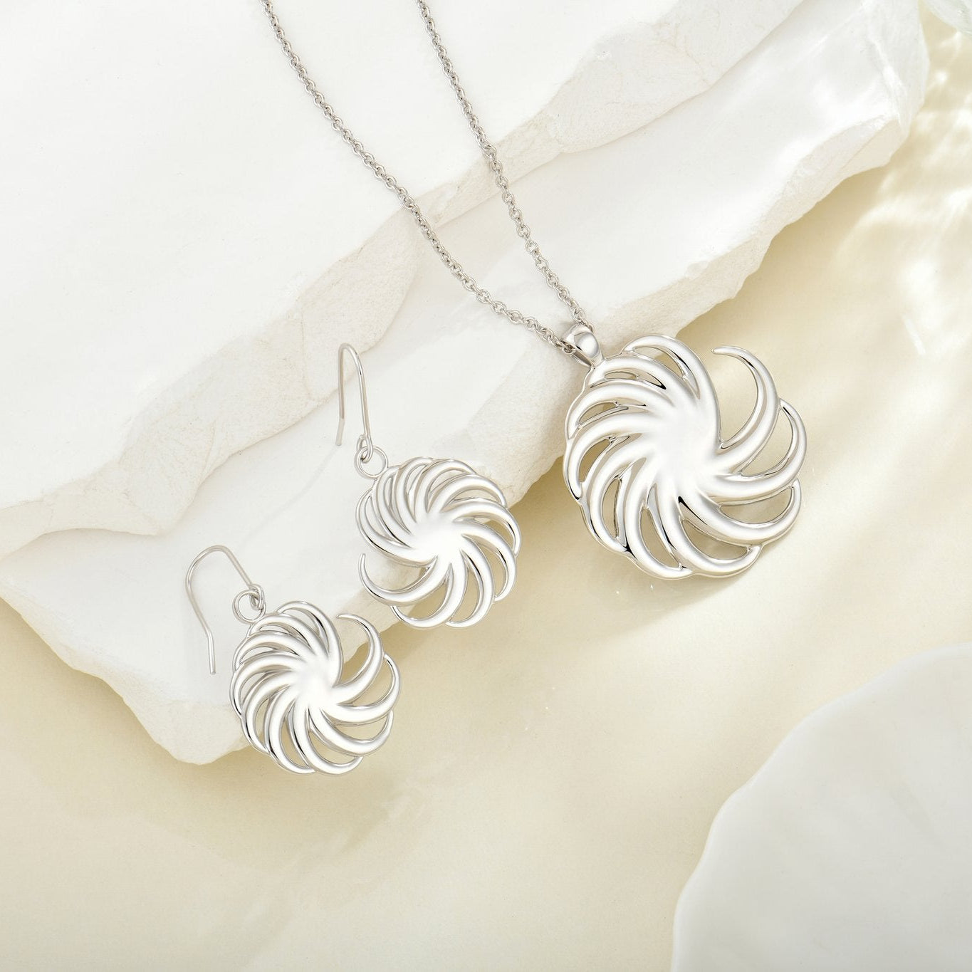 Silver earrings and necklace set on a soft white fabric background