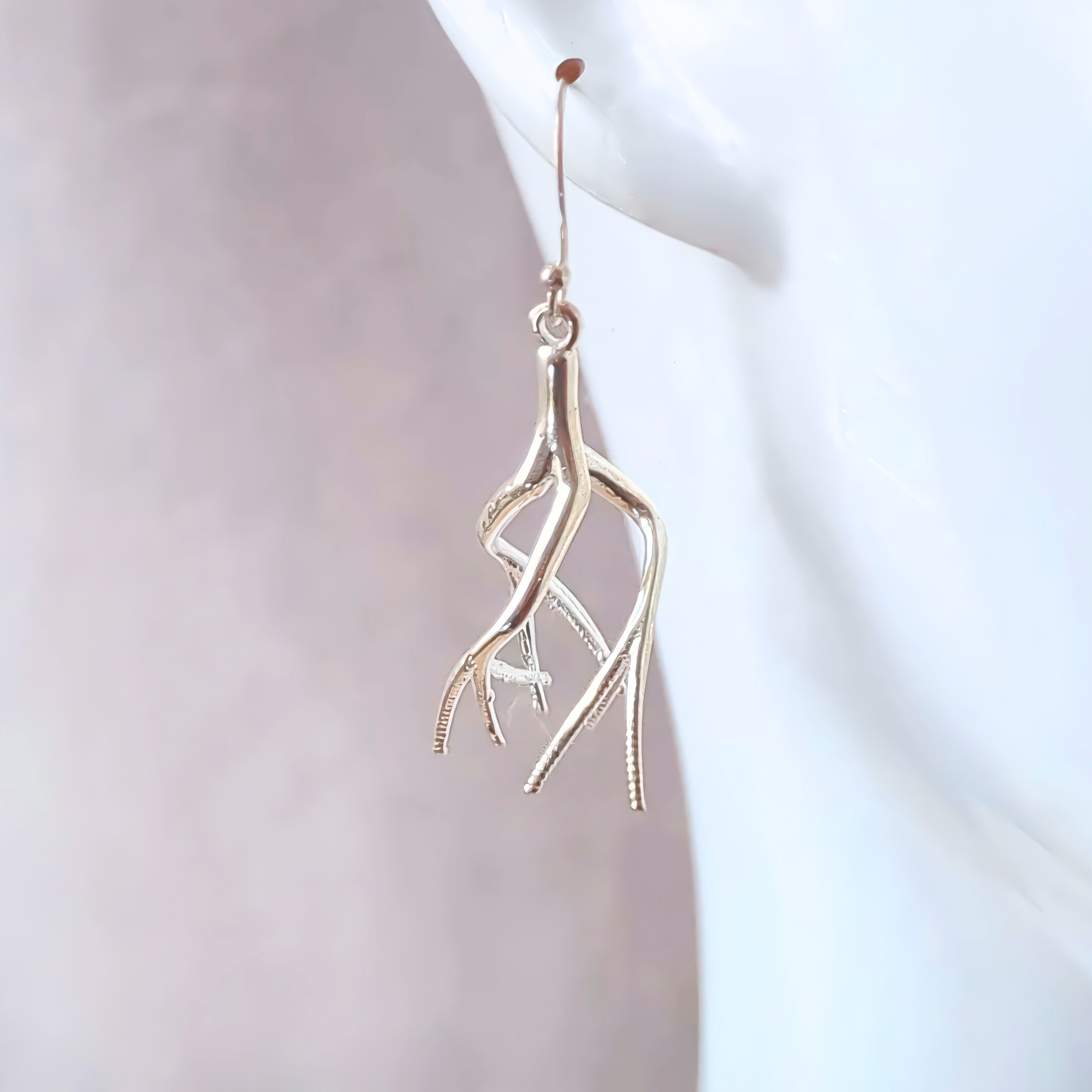 a closeup of a dangling twisted tree earring on a white mannequin in front of a gray backdrop