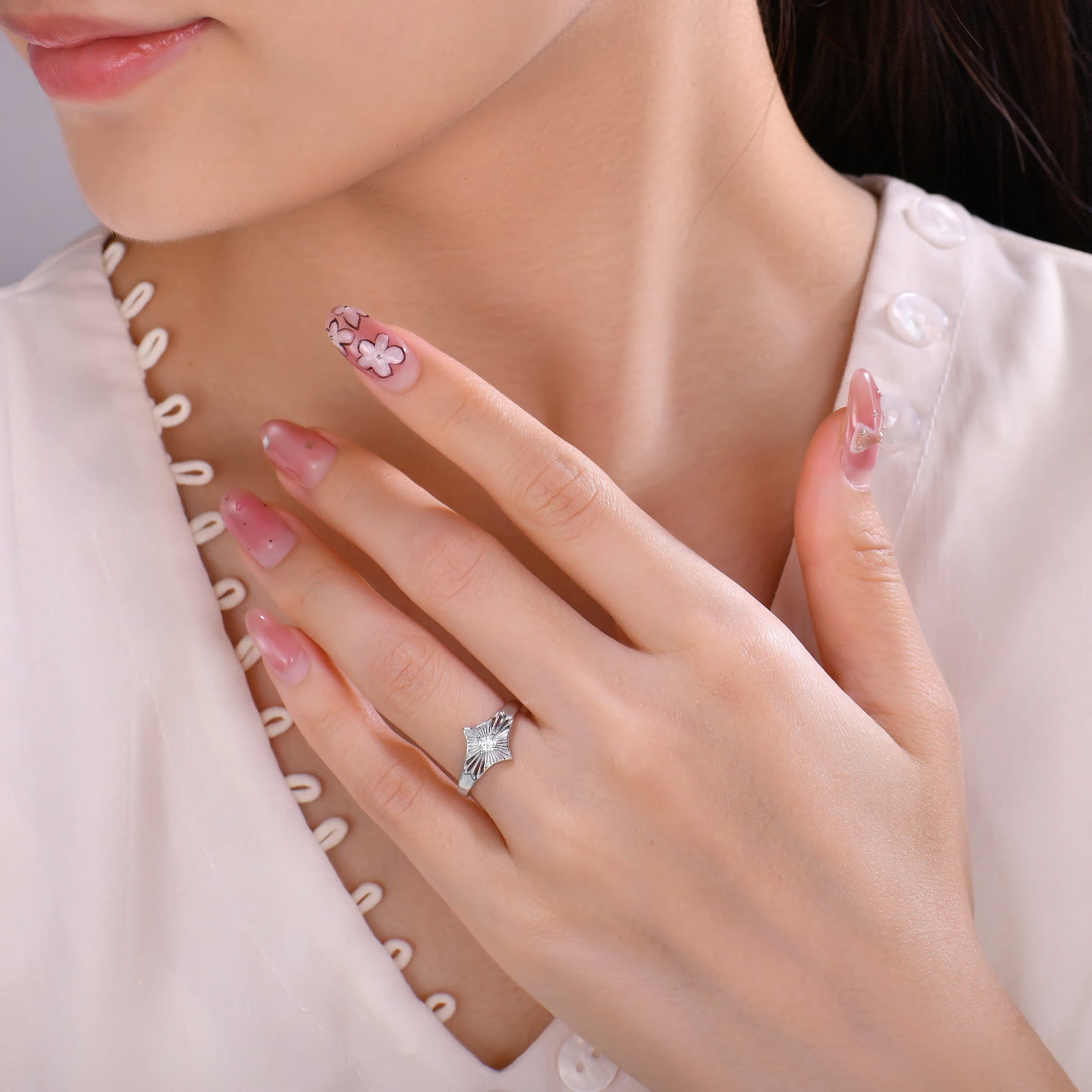 Close-up of a hand wearing a platinum ring with a diamond, against a neutral background.